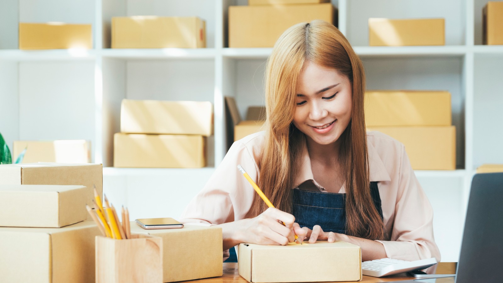 Female small business owner working at her desk, writing on a package.